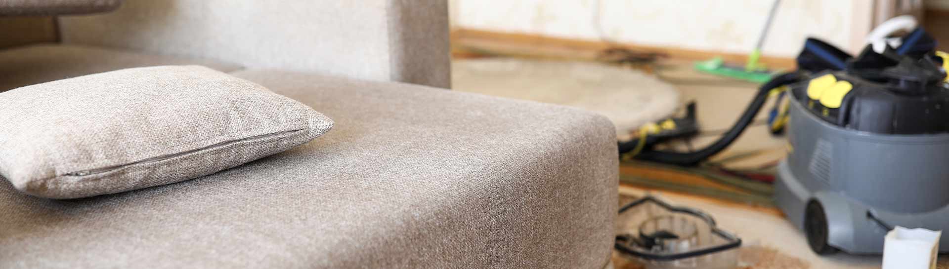 A clean fabric sofa and pillow with professional steam cleaning equipment in the background.