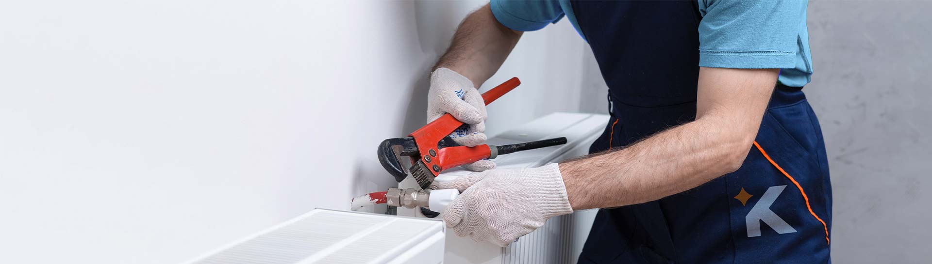 a keeply employee using a red pipe wrench to adjust a valve of a radiator.