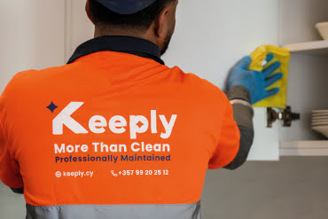 close up of a keeply employee in uniform cleaning the dust from a white closet door of the kitchen.
