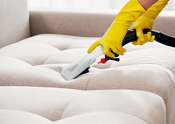close up of a keeply employee vacuuming the furniture of a cough in a living room