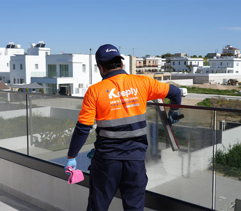 A keeply employee cleans a glass balcony railing with a squeegee in a weekly cleaning service.