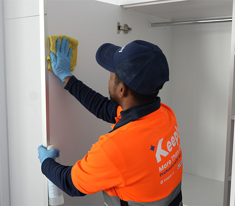 a keeply employee in uniform cleaning and rubbing a white closet door with a cloth and spray in a residential home