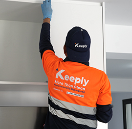 A keeply employee cleaning a kitchen closet door in a weekly cleaning service.