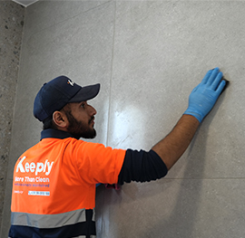 Keeply employee in costume using a cloth to clean a white interior wall in a residential home.