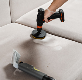 A keeply employee using a power-drill brush attachment to deep-clean a sofa