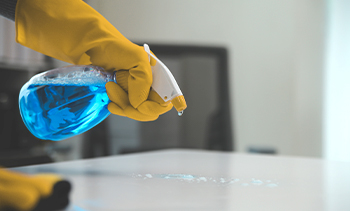 close up of a keeply employee using a spray bottle of specialized chemical to clean a surface.