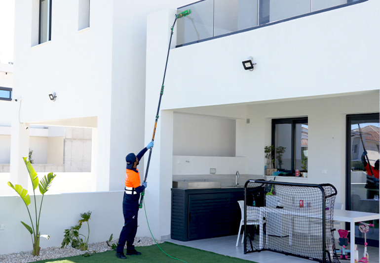 a keeply employee using the ro water machine to clean outdoor glass of a house.