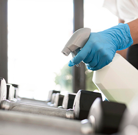 a specialized chemical spray bottle being used by a keeply employee to clean and sanitize dumbells.