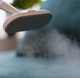 close up of a handheld steamer emitting a cloud of white steam onto a teal fabric surface.