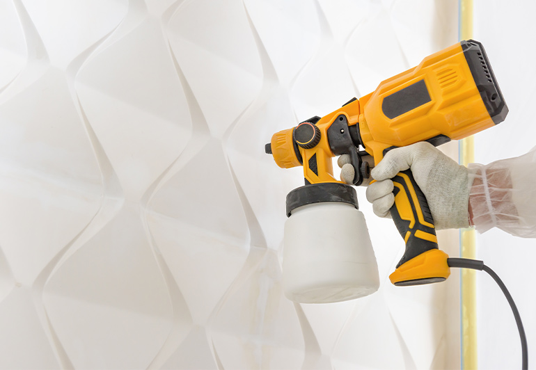 close  up of a paint sprating gun used held by a keeply employee infront of a wall being painted.