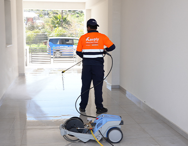 keeply employee using a water pressure washer to clean the floor entrance of a building